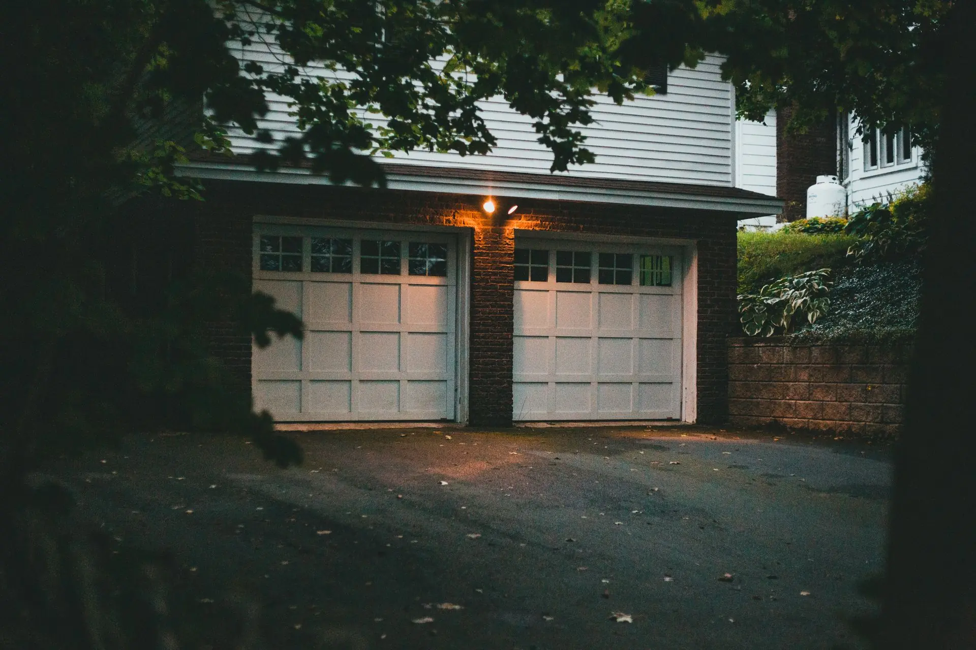Two white garage doors on a brick garage at dusk